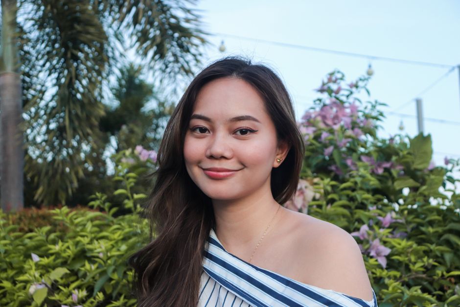 A beautiful woman with an off-shoulder top smiling amidst lush green and floral background