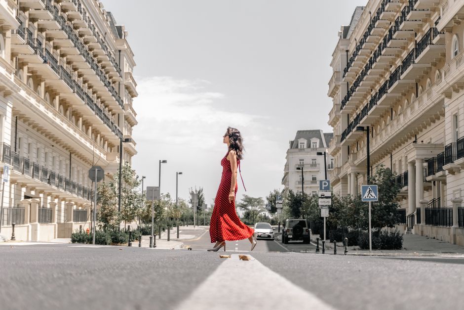 A fashionable woman in a red dress walks between elegant buildings in Baku, Azerbaijan.