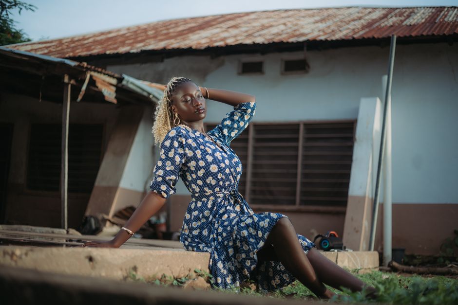 Woman in floral dress posing elegantly outside rustic building.