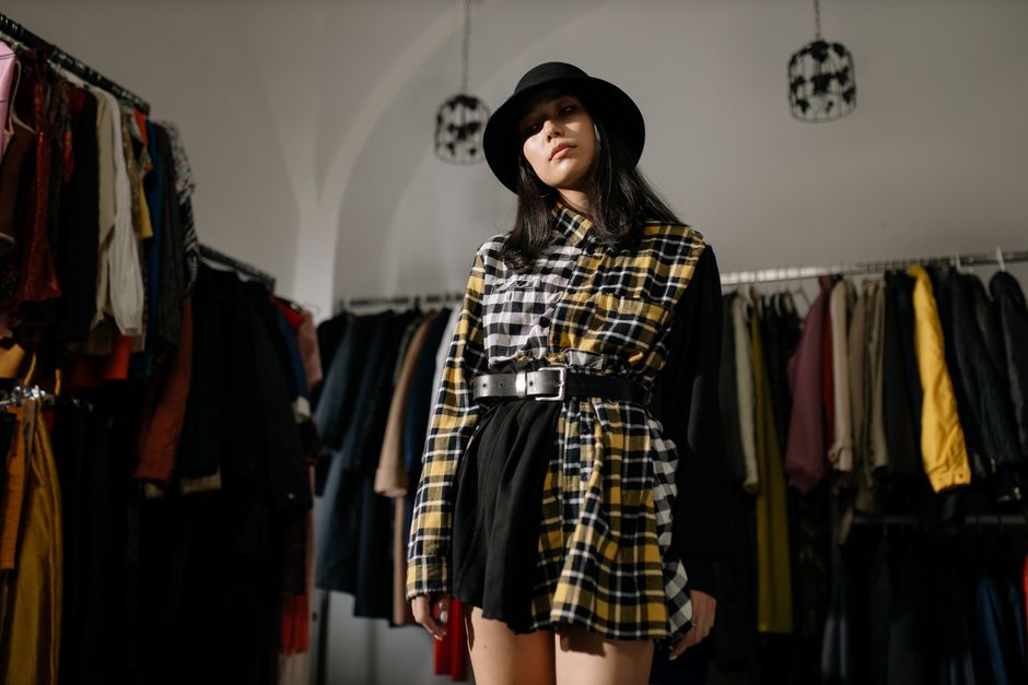 Stylish woman in a plaid outfit and hat posing in a vintage clothing store.