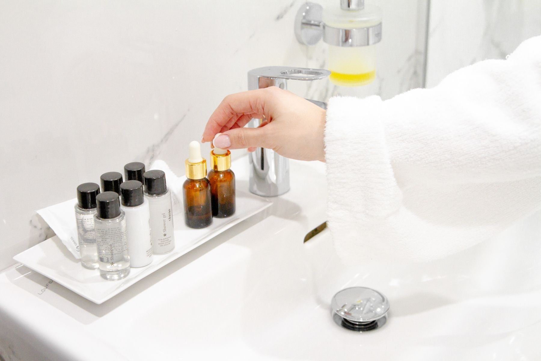 Hand reaching for a serum bottle beside a bathroom sink