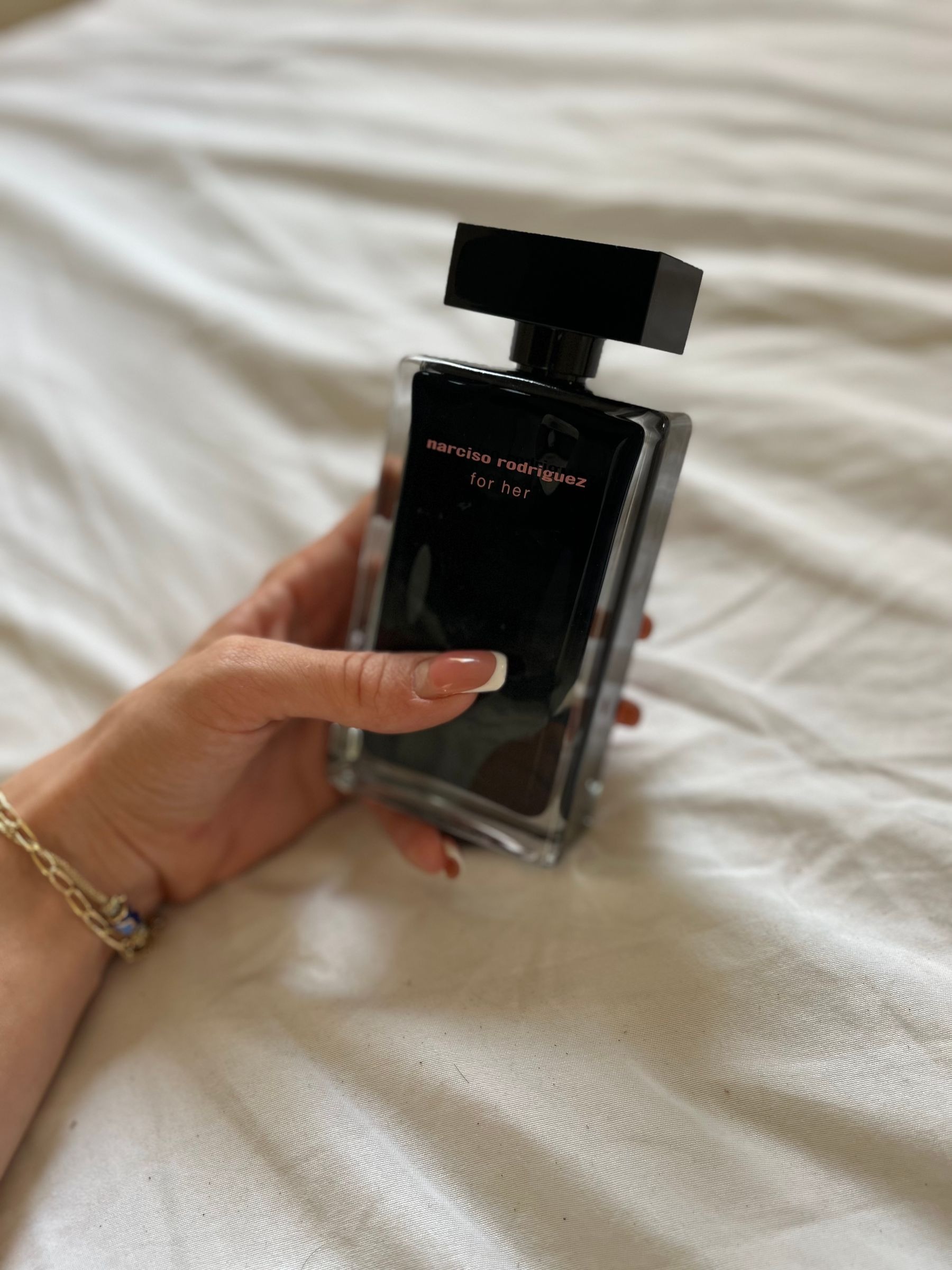 Hand holding a black perfume bottle over white fabric