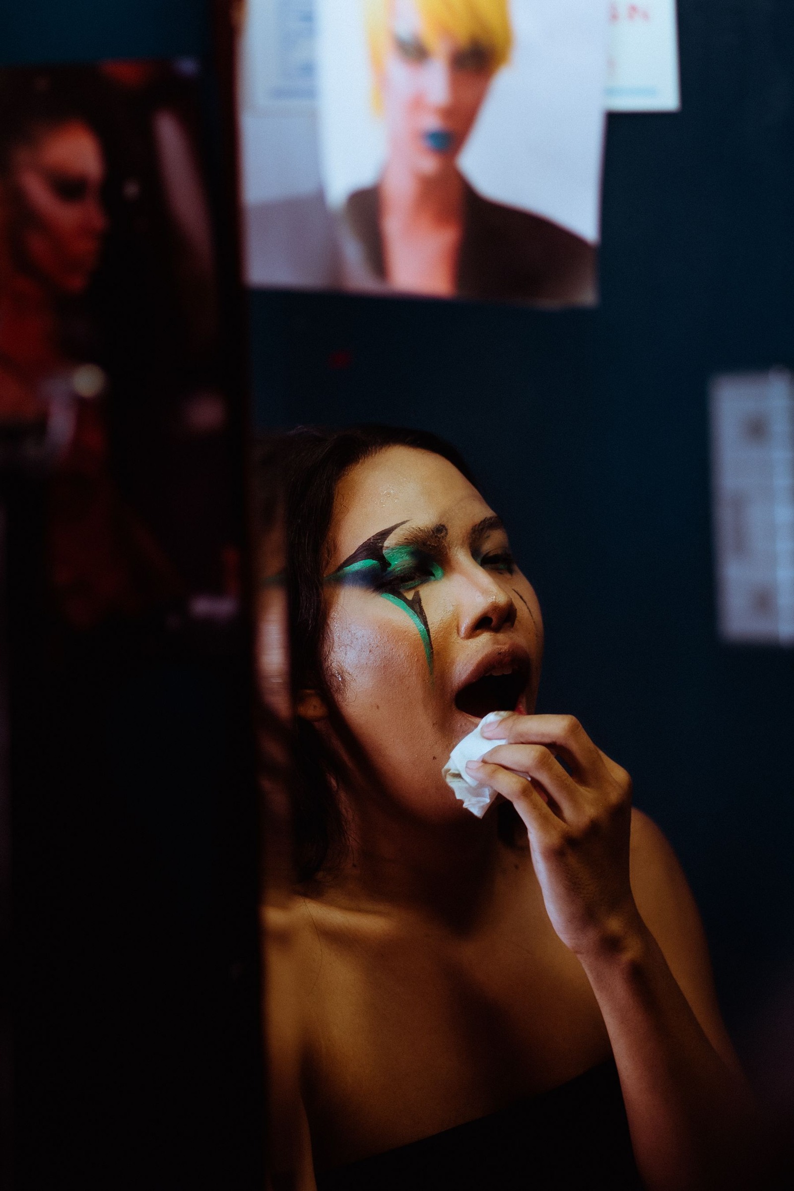 Person removing bright lipstick in front of a dressing-room mirror