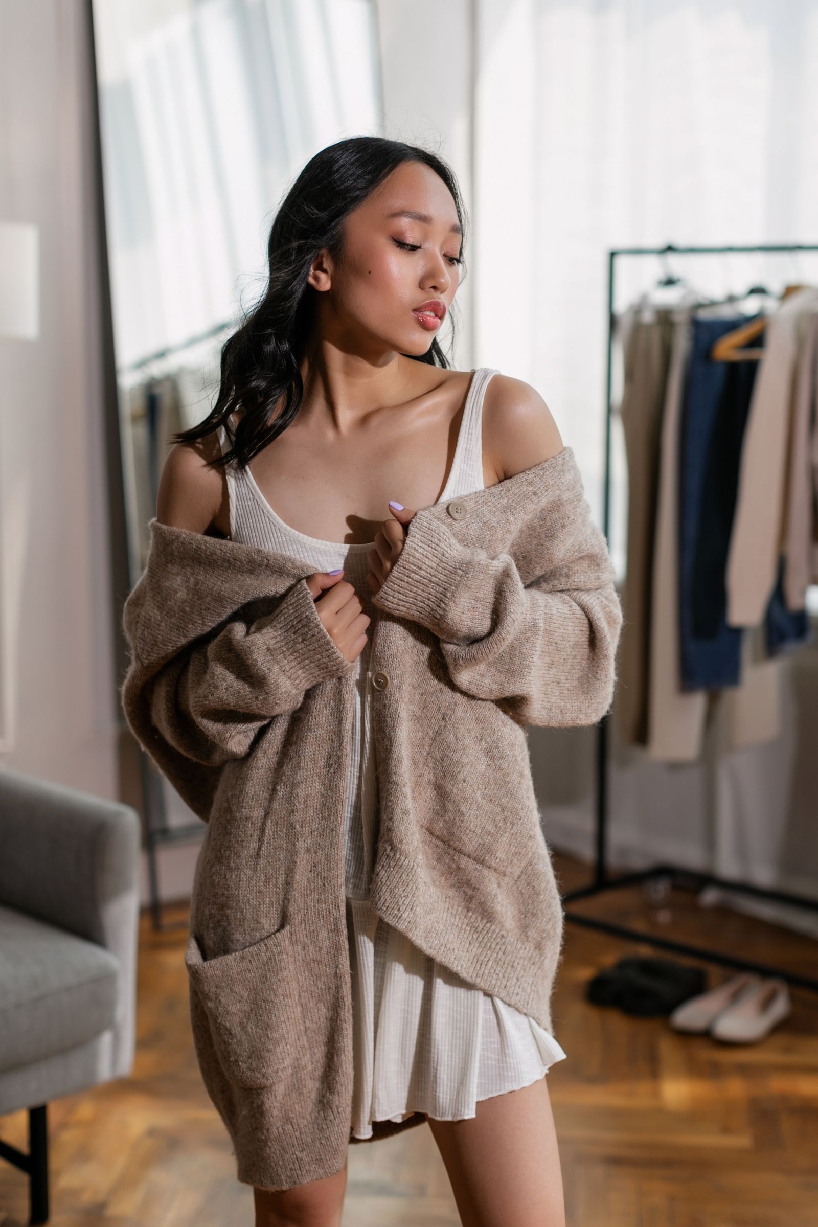 Woman looking down at a white dress worn with a brown cardigan
