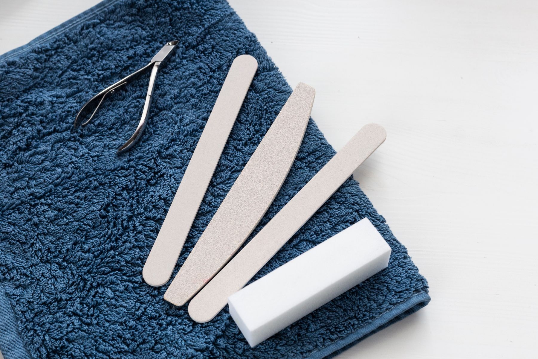 Nail files and a cuticle nipper arranged on a blue towel