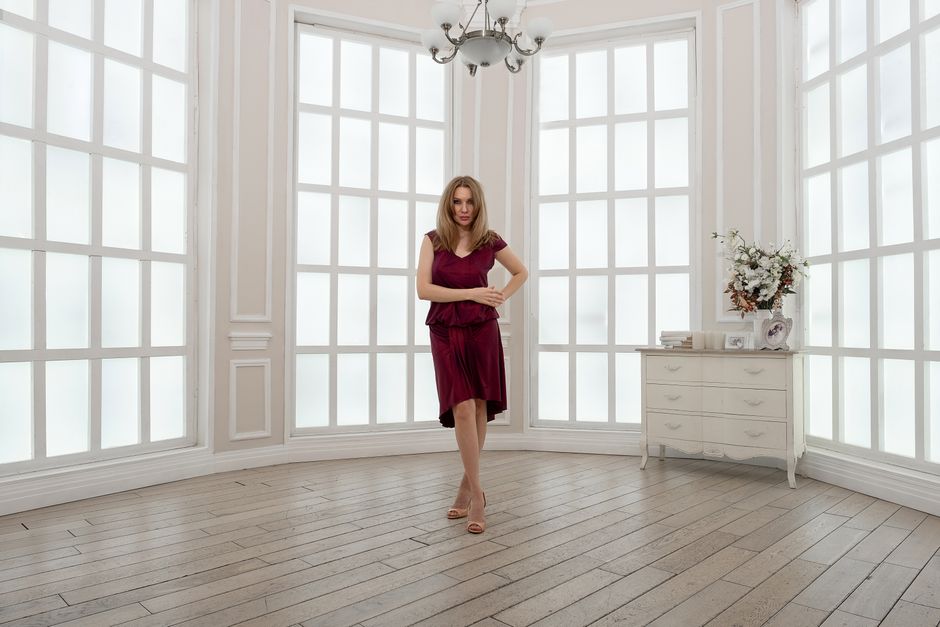 Full body gorgeous female wearing stylish ruby dress standing with hand on waist in light 